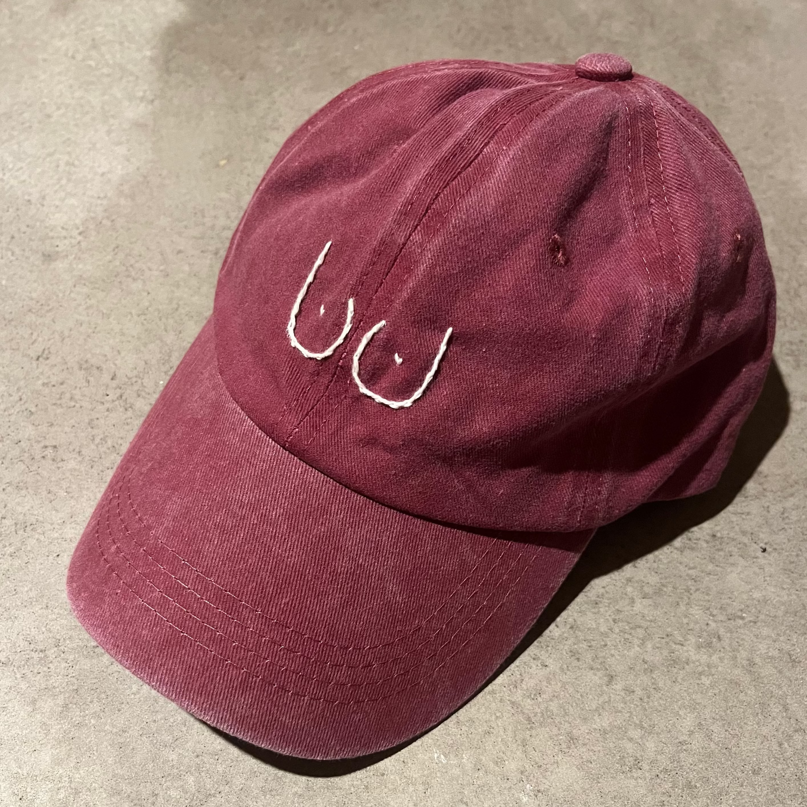 Burgundy cap with white logo on a concrete surface