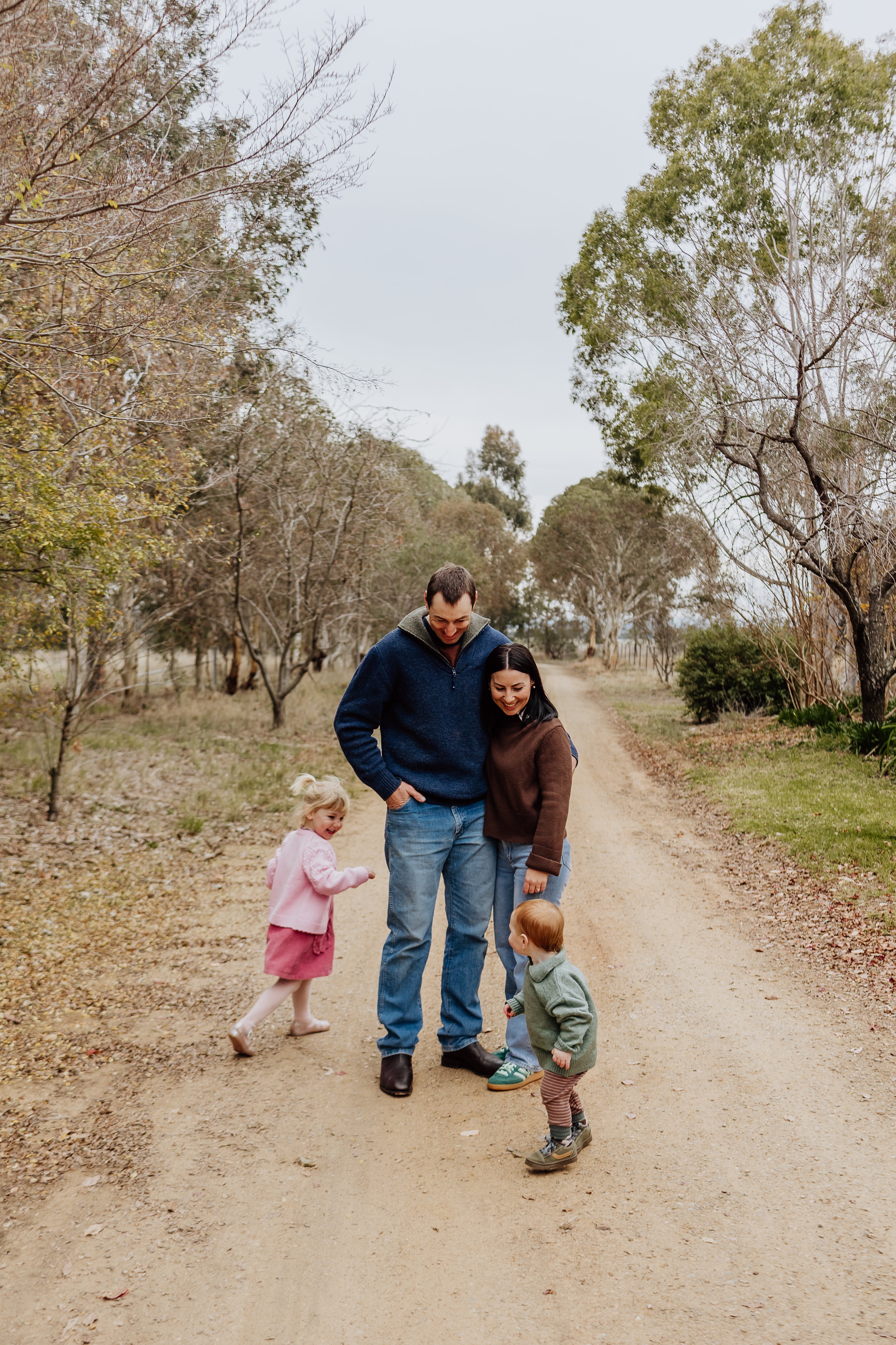 Family of four walking on a dirt path in a park with trees and grass.